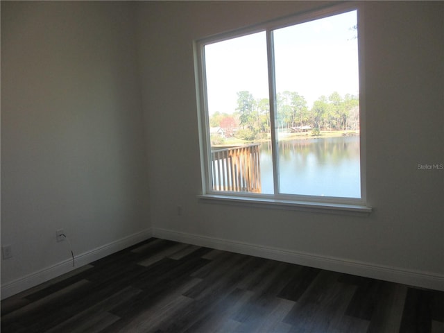 spare room featuring dark wood-style floors, a water view, and baseboards