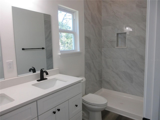 bathroom with toilet, wood finished floors, a sink, a shower stall, and double vanity