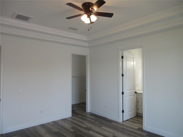 unfurnished bedroom featuring dark wood-type flooring, visible vents, baseboards, a spacious closet, and ornamental molding