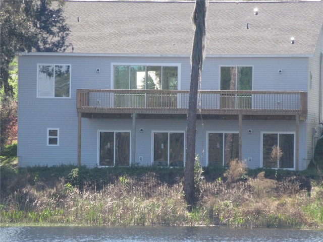 rear view of house featuring a shingled roof and a balcony