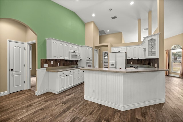 kitchen with backsplash, kitchen peninsula, white appliances, white cabinetry, and high vaulted ceiling