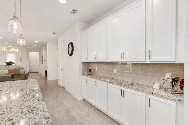 kitchen featuring decorative light fixtures, light stone counters, backsplash, and white cabinets