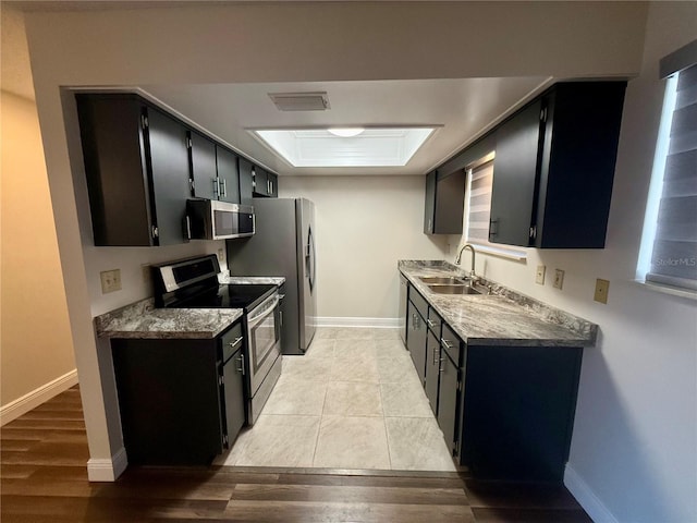 kitchen featuring a tray ceiling, sink, appliances with stainless steel finishes, and light hardwood / wood-style flooring