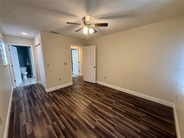 unfurnished bedroom with a textured ceiling, ceiling fan, dark hardwood / wood-style flooring, and ensuite bath