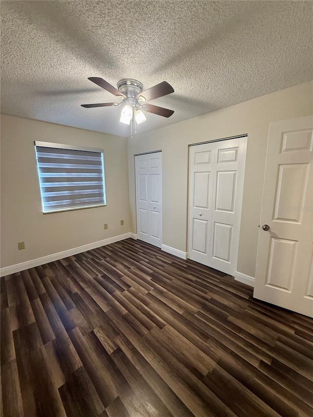 unfurnished bedroom featuring ceiling fan, dark hardwood / wood-style floors, a textured ceiling, and two closets