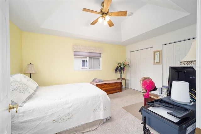 carpeted bedroom with ceiling fan, a raised ceiling, and multiple closets