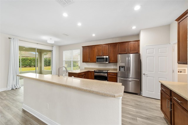 kitchen with a kitchen island with sink, light wood-type flooring, sink, and stainless steel appliances