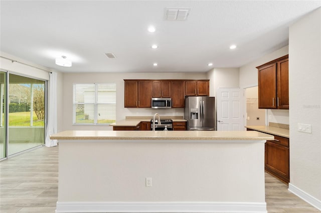 kitchen with light wood-type flooring, appliances with stainless steel finishes, and an island with sink