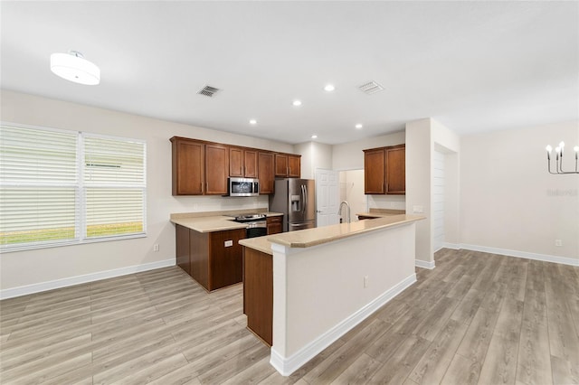 kitchen with kitchen peninsula, light wood-type flooring, appliances with stainless steel finishes, and a chandelier