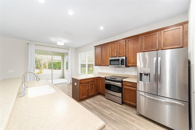 kitchen featuring light wood-type flooring, kitchen peninsula, sink, and stainless steel appliances