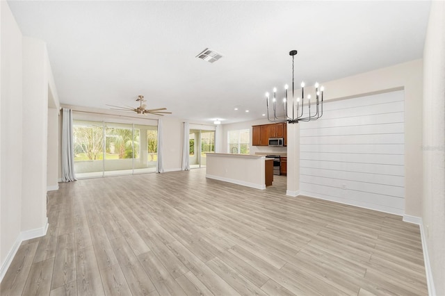 unfurnished living room featuring ceiling fan with notable chandelier, light hardwood / wood-style floors, and wood walls