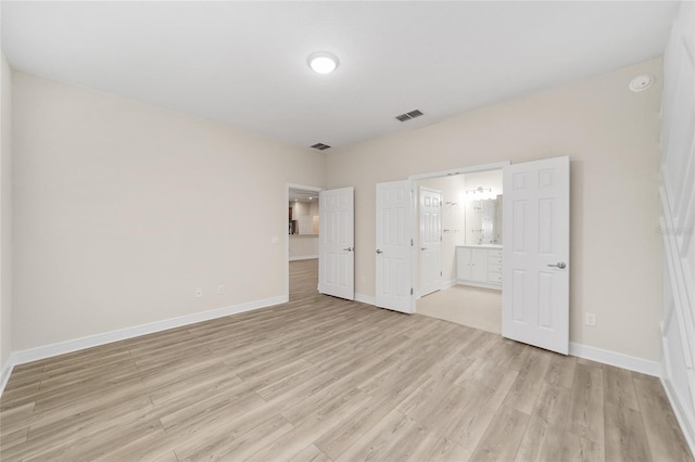 unfurnished bedroom featuring ensuite bathroom and light hardwood / wood-style flooring