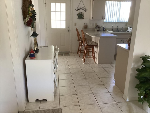 kitchen with white cabinets, sink, kitchen peninsula, a breakfast bar, and light tile patterned floors