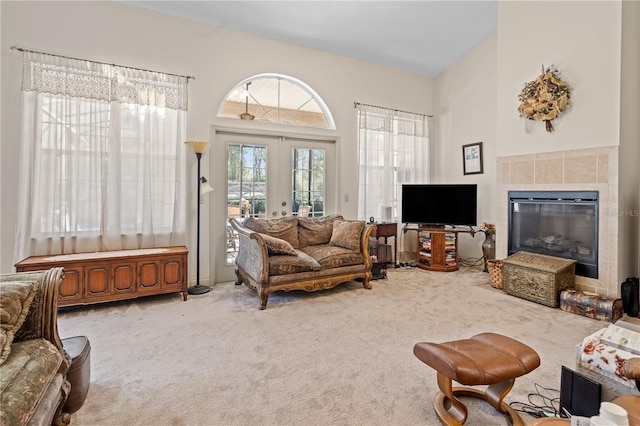 carpeted living room featuring a tiled fireplace, french doors, and a high ceiling