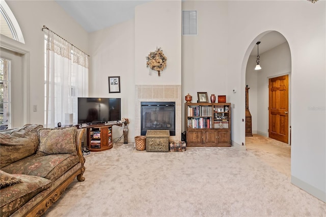 carpeted living room with a tile fireplace and a towering ceiling