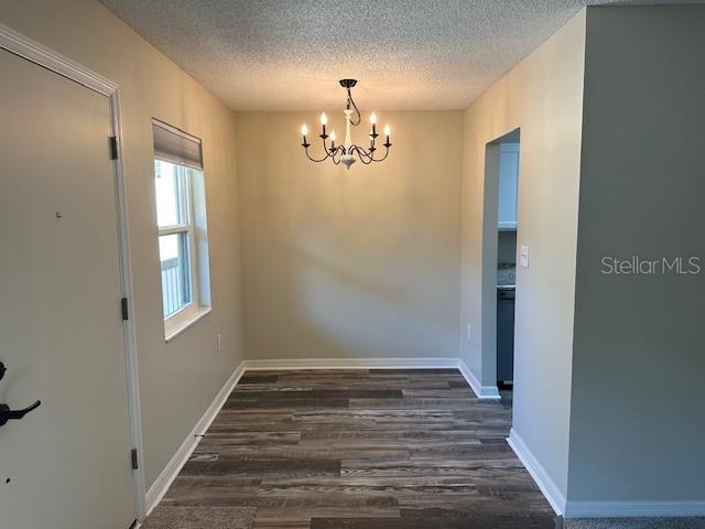 unfurnished dining area featuring a textured ceiling, a chandelier, and dark hardwood / wood-style floors