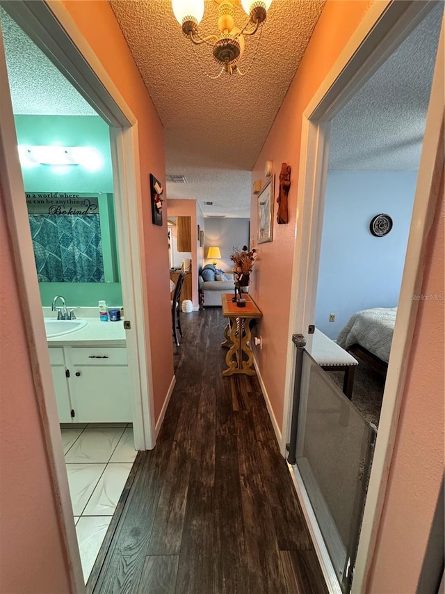 hall with sink, a textured ceiling, dark hardwood / wood-style flooring, and a notable chandelier