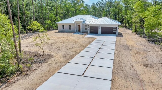 6877 SW 131st Cir, Ocala, FL 34481 - view of front of home featuring a garage, metal roof, driveway, a wooded view, and stucco siding