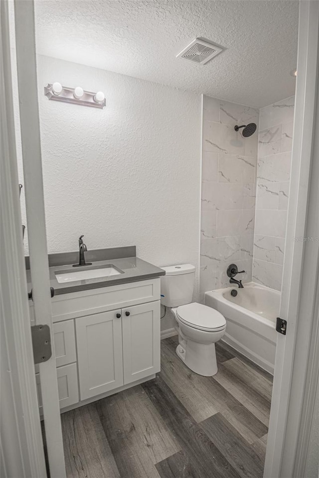 full bathroom with toilet, vanity, tiled shower / bath, hardwood / wood-style floors, and a textured ceiling