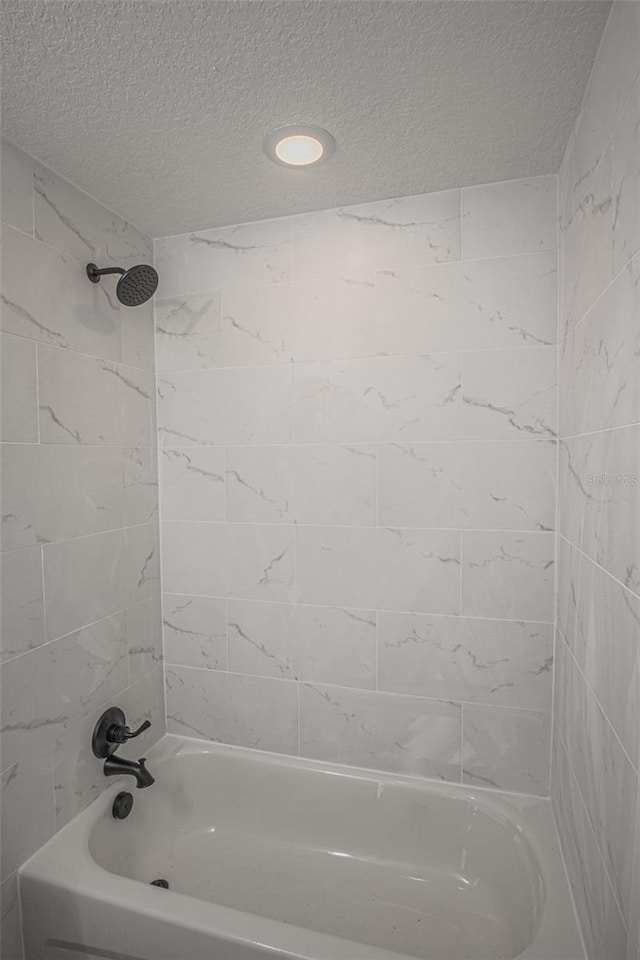 bathroom with tiled shower / bath combo and a textured ceiling