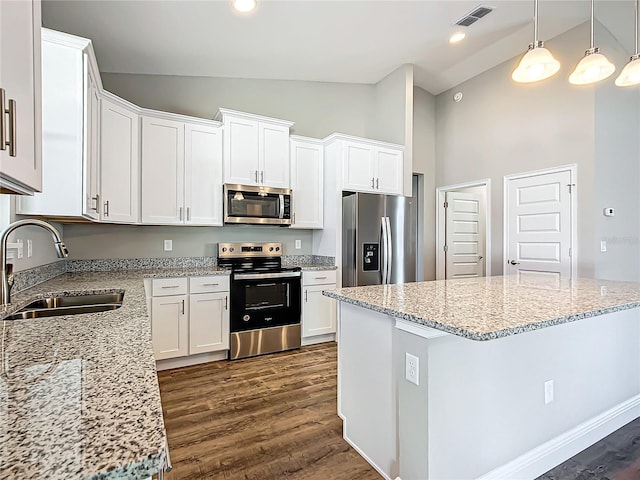 kitchen with sink, appliances with stainless steel finishes, white cabinetry, light stone counters, and a kitchen island