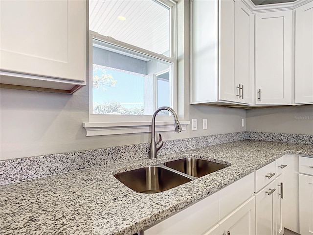 kitchen featuring sink, light stone countertops, and white cabinets