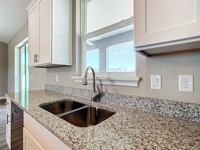 kitchen with sink, white cabinetry, dishwasher, light stone countertops, and hardwood / wood-style floors