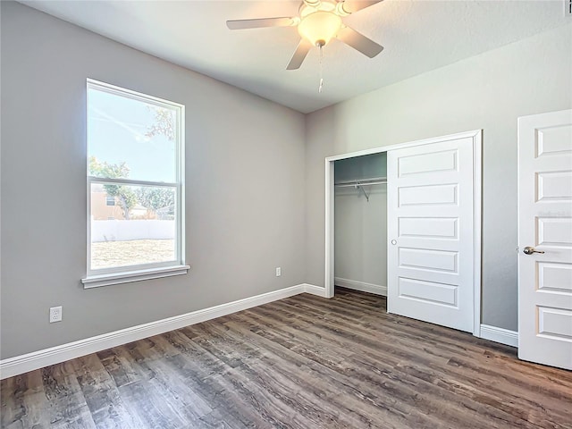 unfurnished bedroom featuring multiple windows, dark hardwood / wood-style flooring, ceiling fan, and a closet