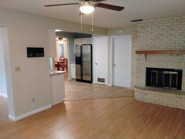 unfurnished living room featuring ceiling fan, a brick fireplace, and light hardwood / wood-style floors