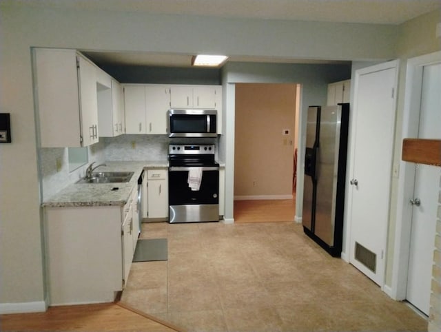 kitchen featuring appliances with stainless steel finishes, white cabinetry, decorative backsplash, sink, and light stone counters