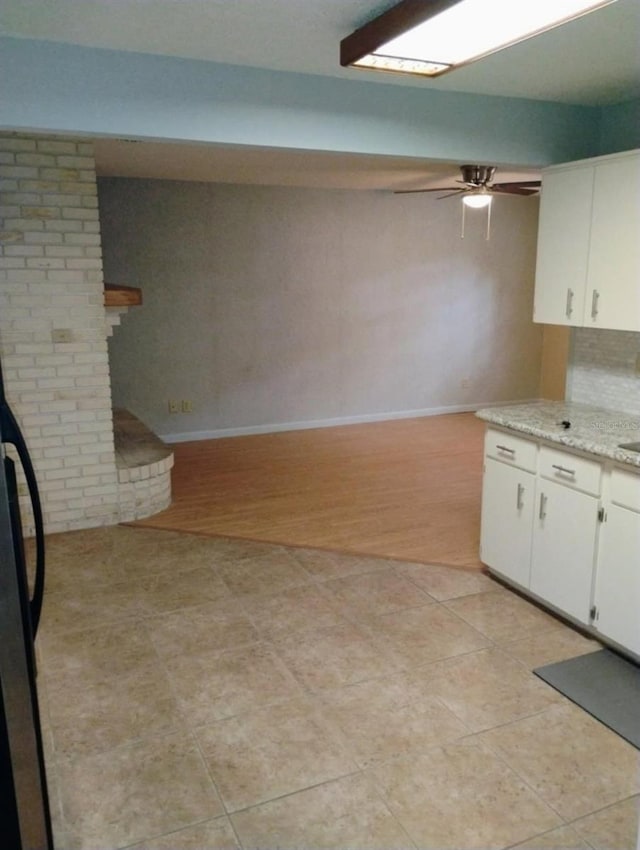 kitchen featuring white cabinetry, black refrigerator, ceiling fan, light wood-type flooring, and light stone countertops