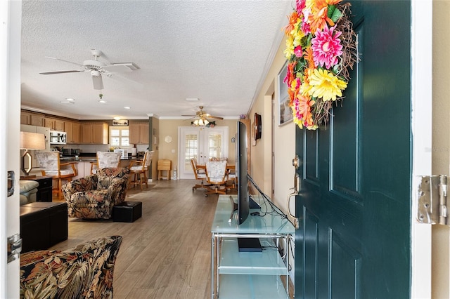 foyer entrance with light wood-type flooring, ornamental molding, a textured ceiling, and french doors