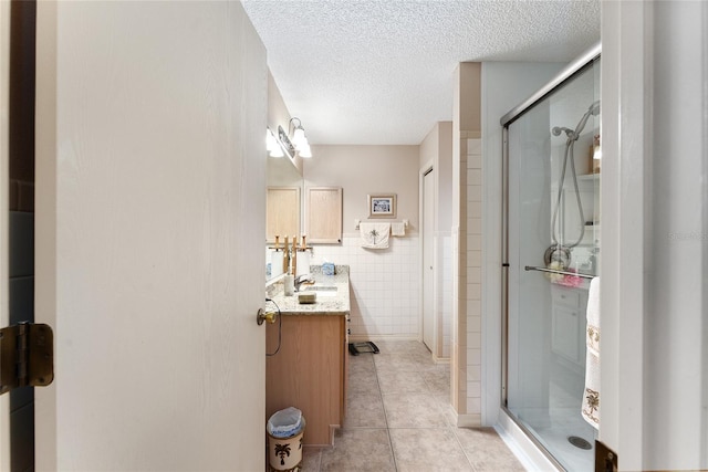 bathroom with a textured ceiling, tile patterned flooring, vanity, tile walls, and walk in shower