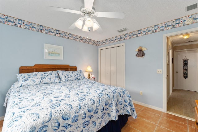 bedroom with a textured ceiling, a closet, ornamental molding, light tile patterned flooring, and ceiling fan