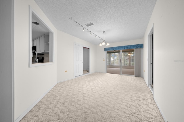 unfurnished room featuring light colored carpet, a textured ceiling, a notable chandelier, and rail lighting