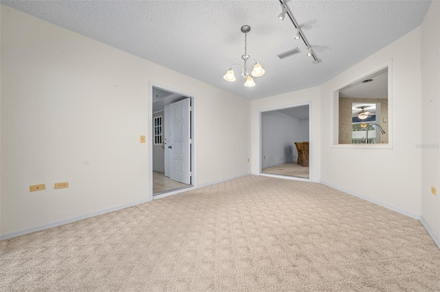 carpeted spare room featuring an inviting chandelier, track lighting, and a textured ceiling