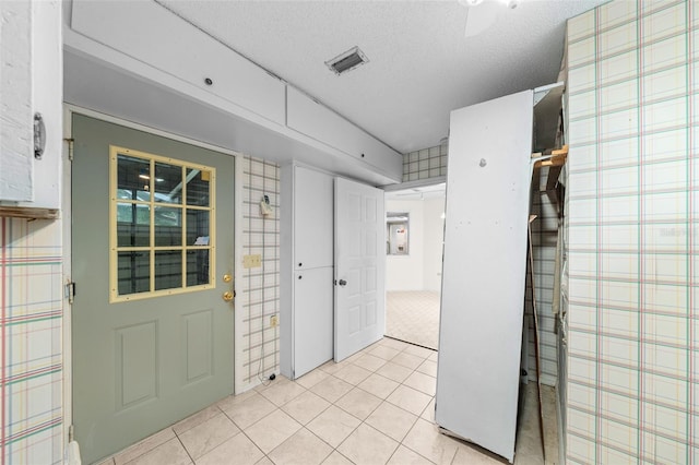 entrance foyer with ceiling fan, light tile patterned flooring, and a textured ceiling