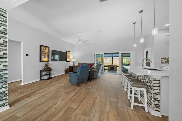 living room with ceiling fan, a towering ceiling, sink, and light hardwood / wood-style flooring