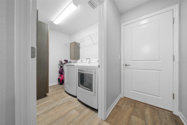 laundry area with separate washer and dryer, a textured ceiling, and light hardwood / wood-style flooring