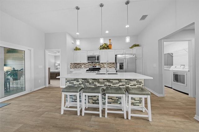 kitchen featuring white cabinets, stainless steel appliances, washing machine and clothes dryer, sink, and hanging light fixtures