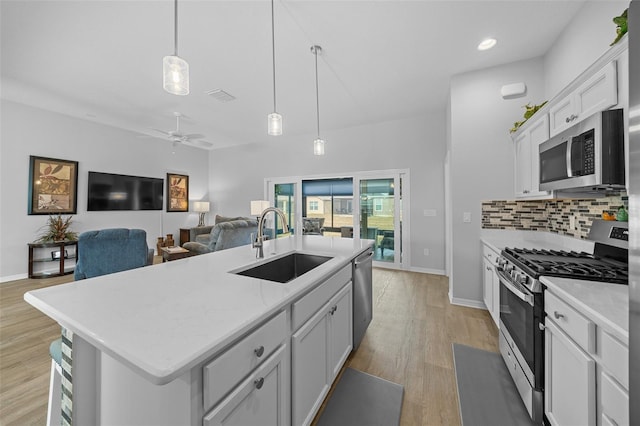 kitchen with appliances with stainless steel finishes, decorative light fixtures, sink, backsplash, and a kitchen island with sink