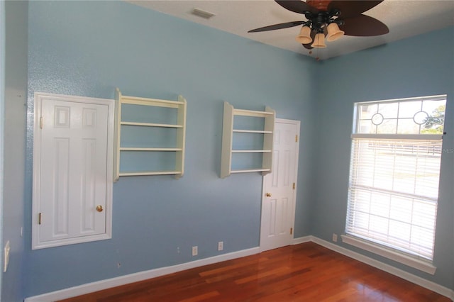 spare room with dark wood-type flooring, ceiling fan, and a healthy amount of sunlight