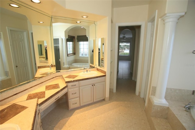 bathroom with a wealth of natural light, decorative columns, and tiled bath