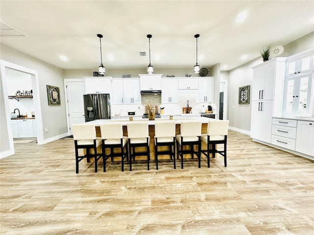 kitchen featuring stainless steel fridge with ice dispenser, a breakfast bar area, hanging light fixtures, and an island with sink