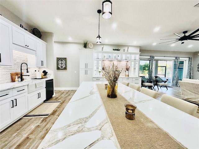 kitchen featuring black dishwasher, white cabinets, light stone countertops, pendant lighting, and light hardwood / wood-style flooring