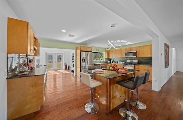 kitchen with appliances with stainless steel finishes, a kitchen island, french doors, a breakfast bar, and light hardwood / wood-style flooring