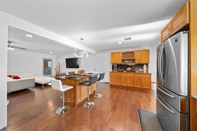 kitchen featuring wood-type flooring, tasteful backsplash, hanging light fixtures, stainless steel fridge, and a breakfast bar