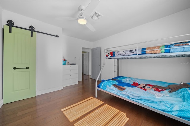 bedroom with ceiling fan, a barn door, and dark hardwood / wood-style floors