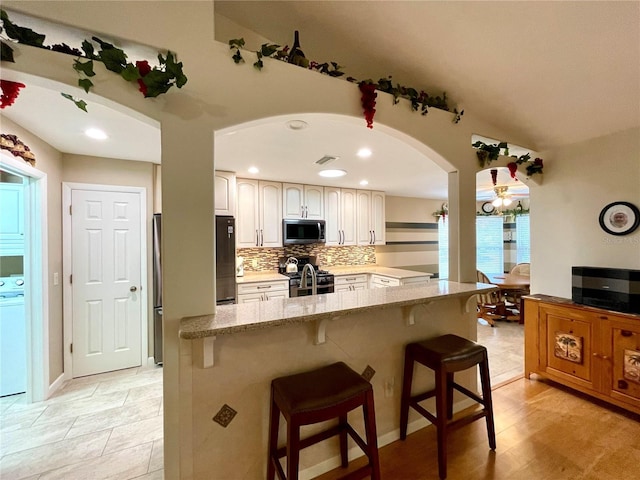 kitchen with a kitchen breakfast bar, stainless steel appliances, light stone counters, white cabinetry, and kitchen peninsula