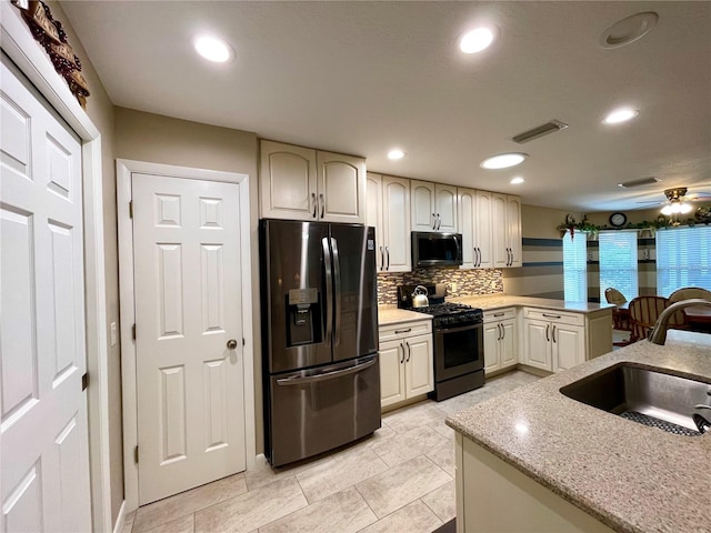 kitchen with light stone countertops, gas stove, stainless steel fridge, backsplash, and sink